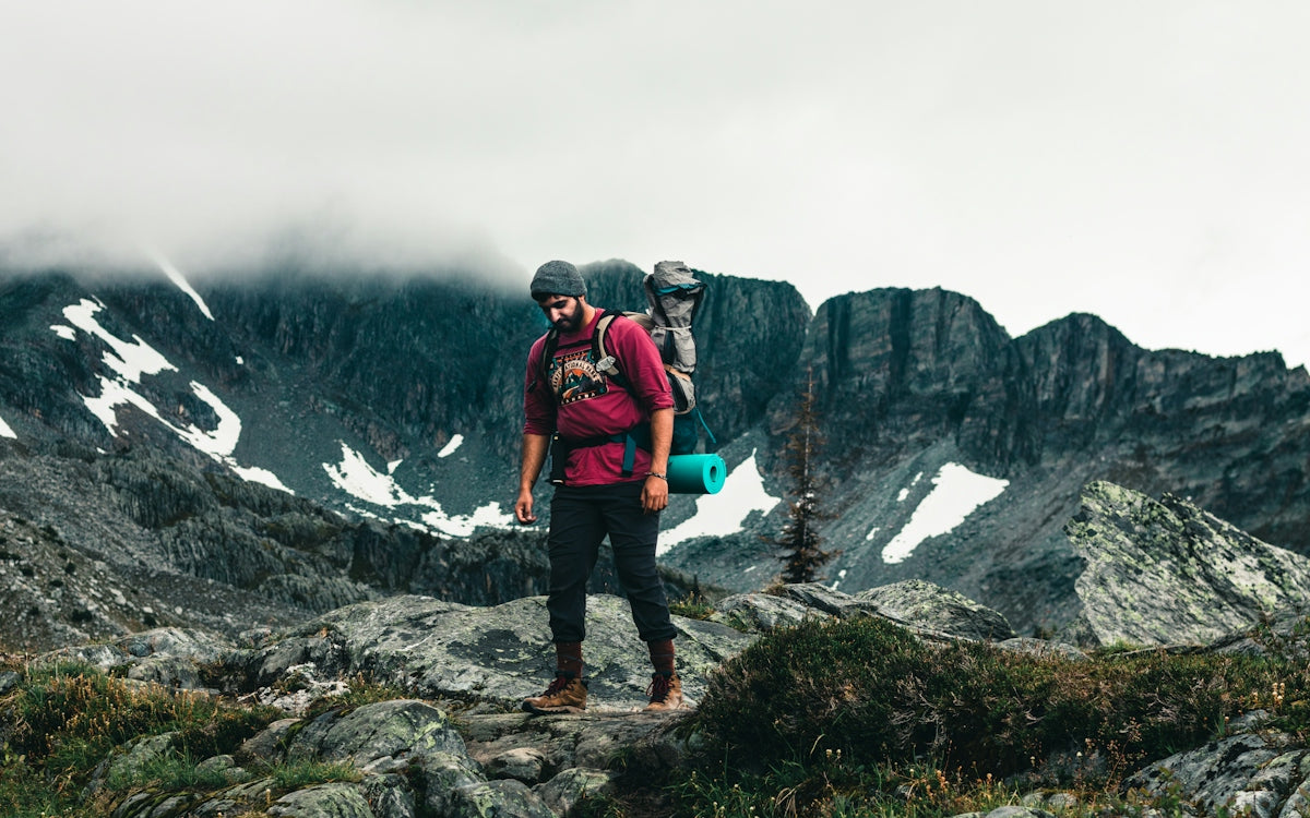 man in red jacket and black pants standing on rocky mountain during daytime