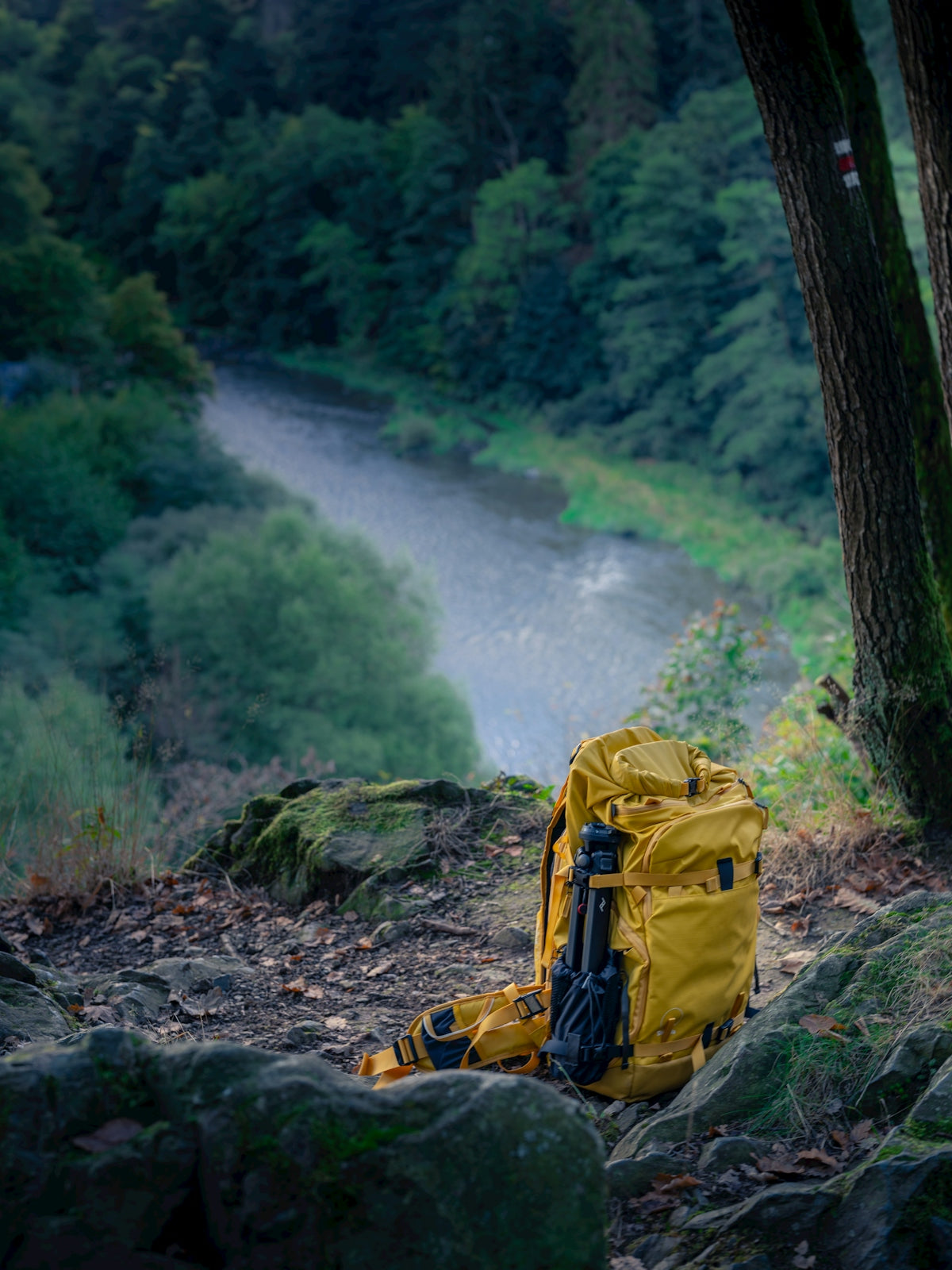 Yellow backpack rests on rocky ground overlooking river.