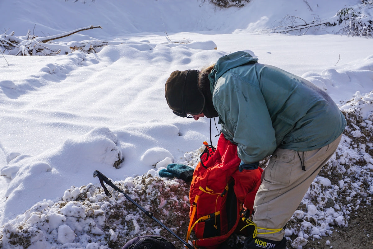 Person in winter gear packing red backpack in snow.