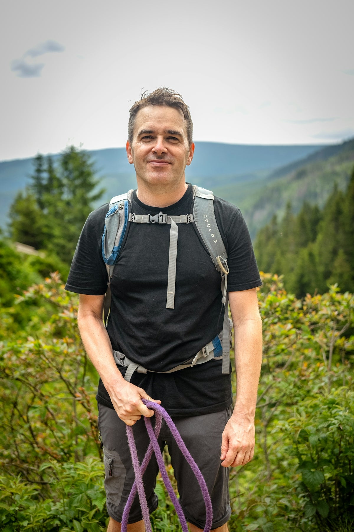 Man with backpack holding rope in forest