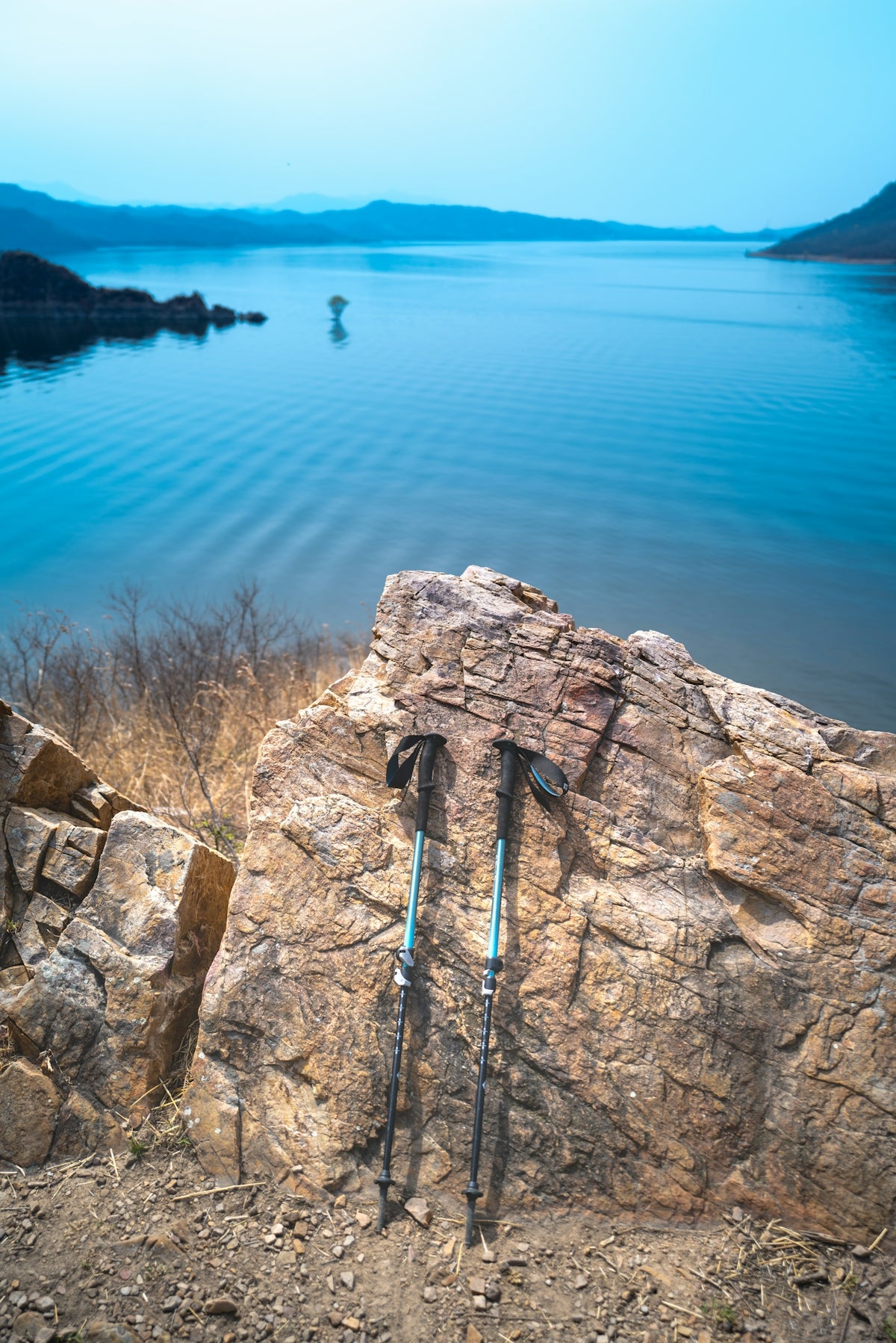 Trekking poles rest on a rock overlooking a serene lake.