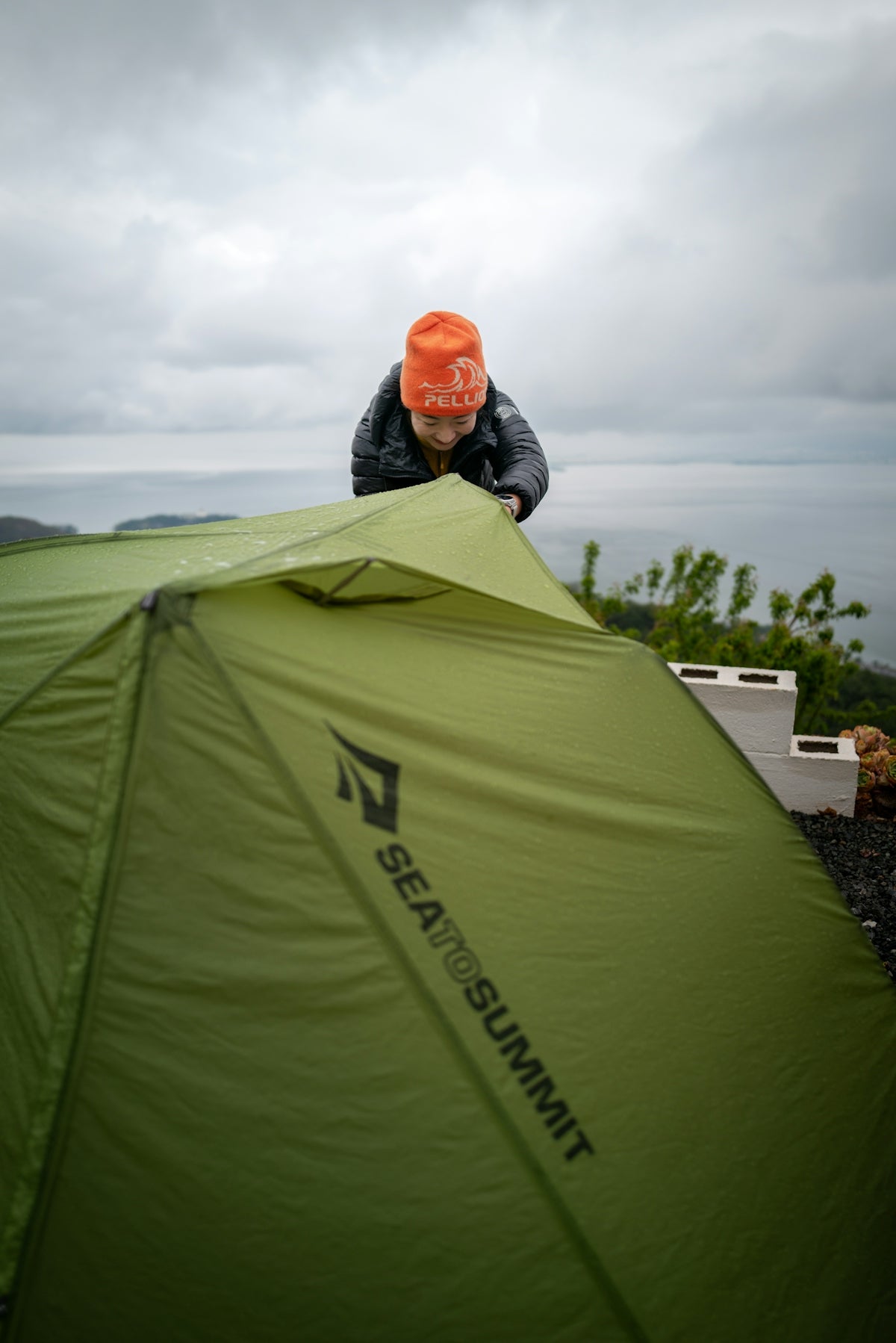 Person setting up a green tent outdoors near the ocean