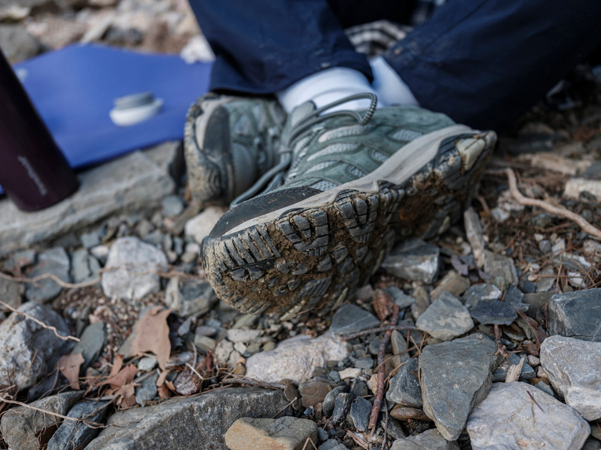 Muddy trekking boots resting on rocky ground.