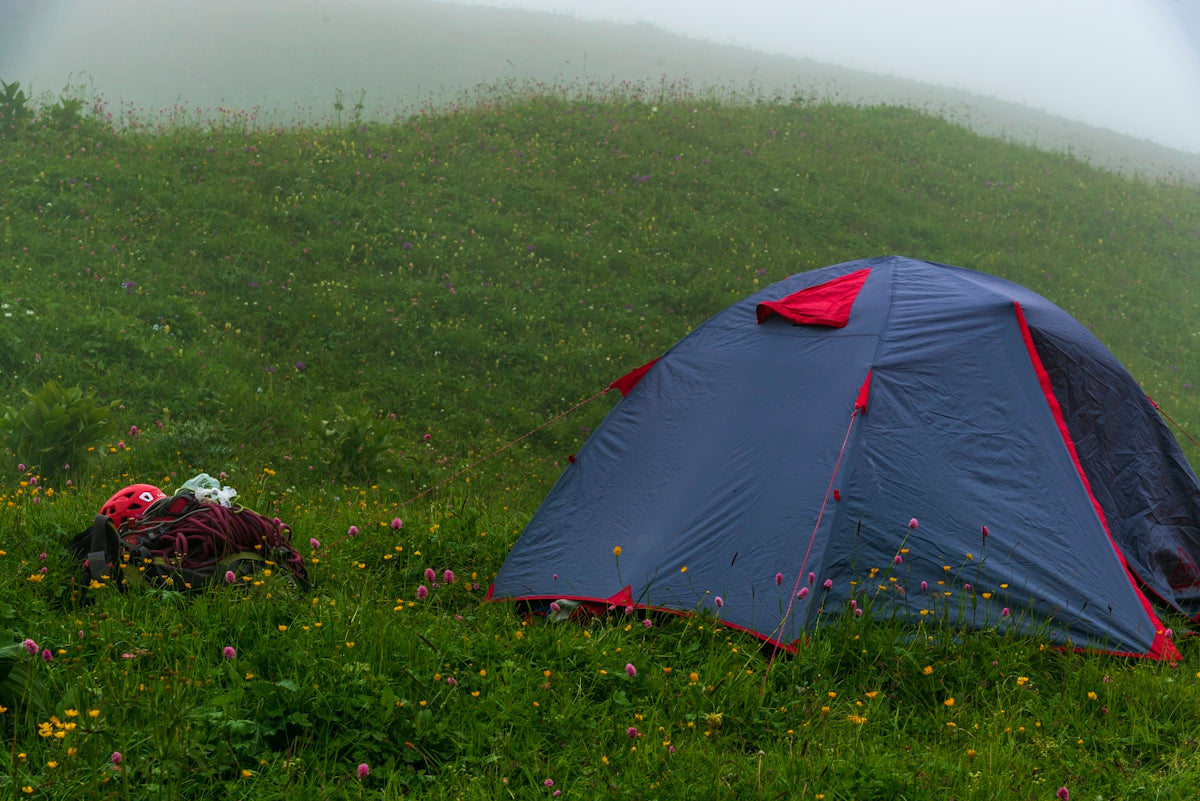 Blue tent on a misty green hillside with camping gear