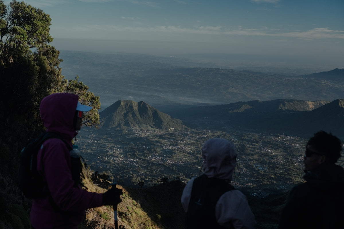 Three people in hiking gear looking out over a vast mountain valley landscape.
