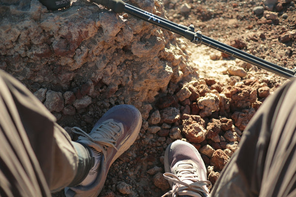 A person wearing hiking shoes on a rocky trail with a trekking pole